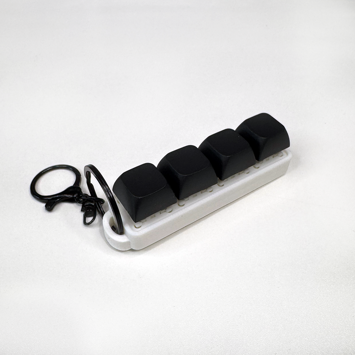 A white four-button clicker fidget keychain with a keychain ring, made with a biodegradable, plant-based plastic.
