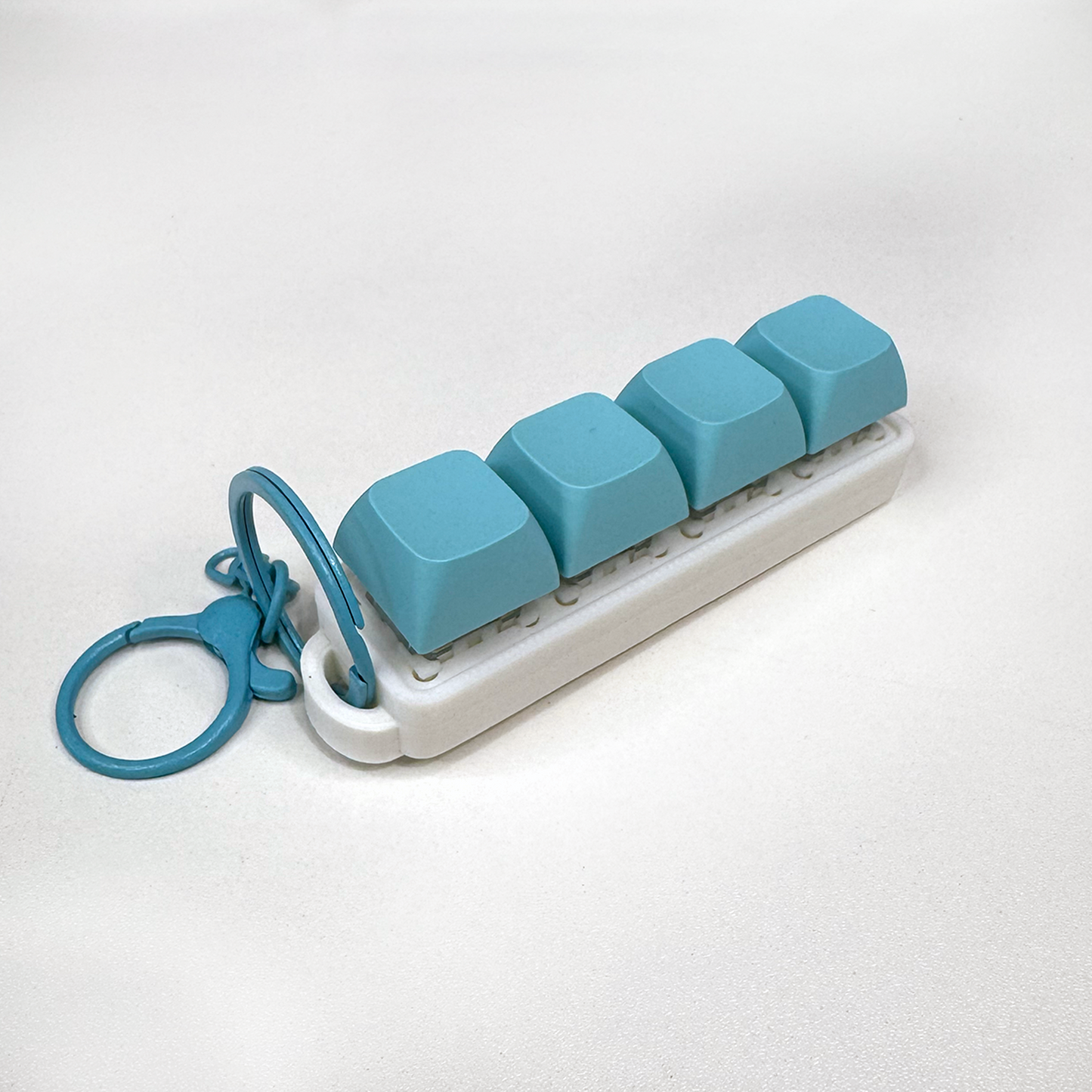 A white four-button clicker fidget keychain with a keychain ring, made with a biodegradable, plant-based plastic.