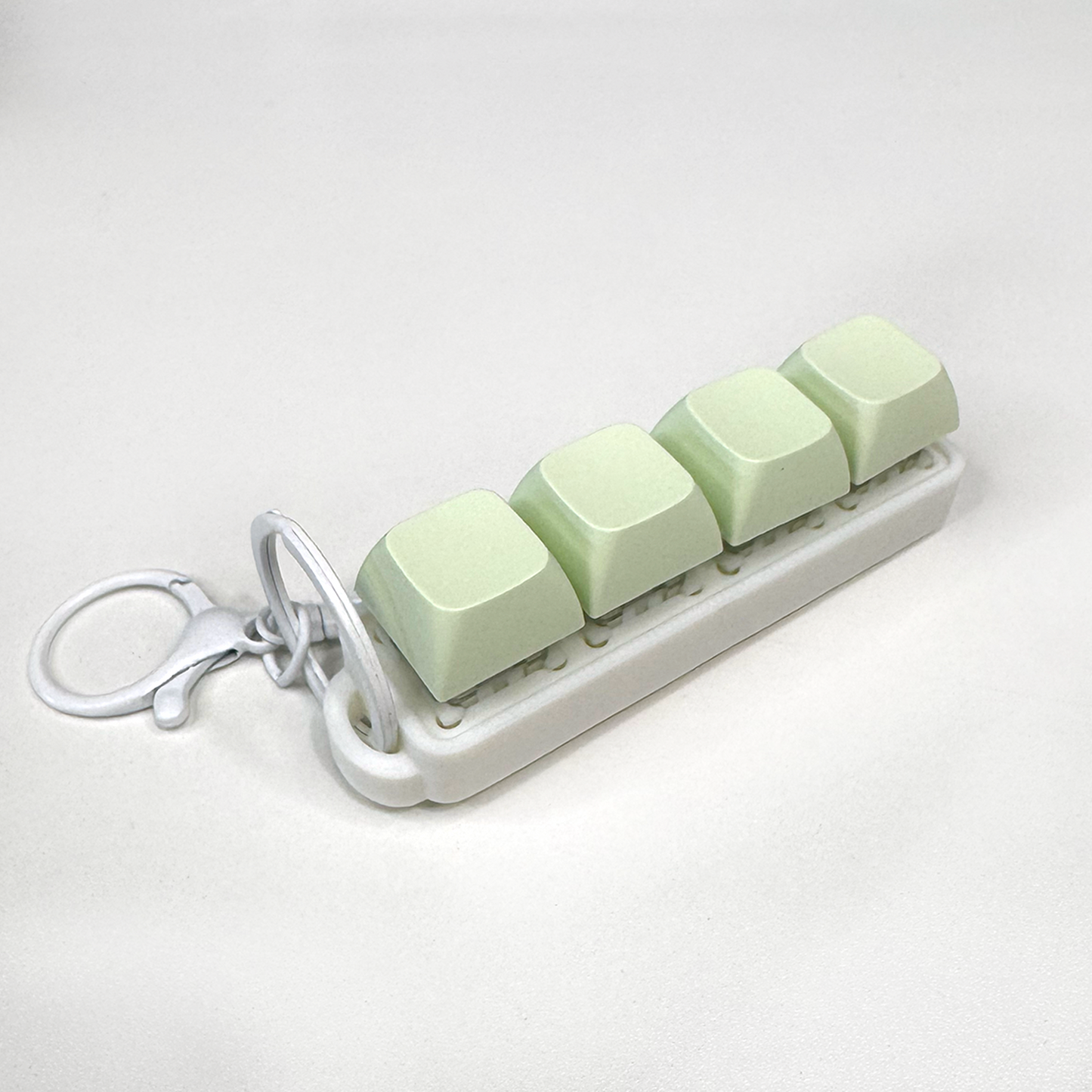 A white four-button clicker fidget keychain with a keychain ring, made with a biodegradable, plant-based plastic.