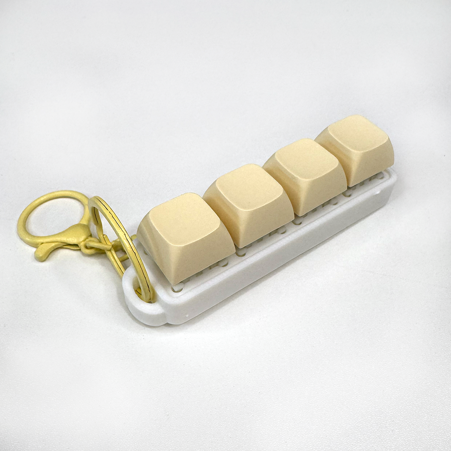 A white four-button clicker fidget keychain with a keychain ring, made with a biodegradable, plant-based plastic.