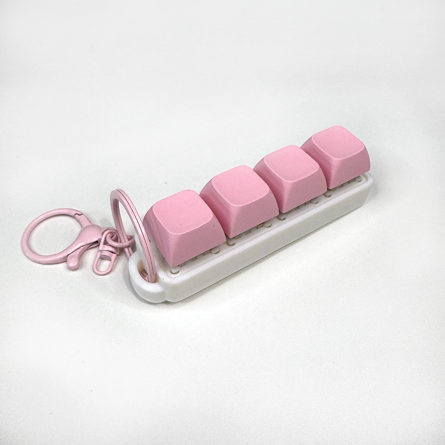 A white four-button clicker fidget keychain with a keychain ring, made with a biodegradable, plant-based plastic.