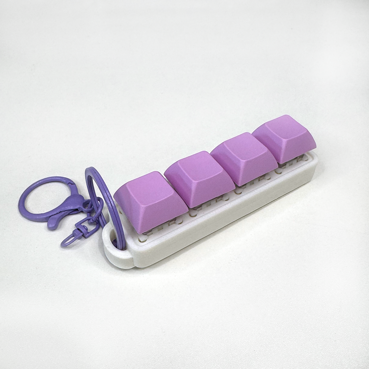 A white four-button clicker fidget keychain with a keychain ring, made with a biodegradable, plant-based plastic.