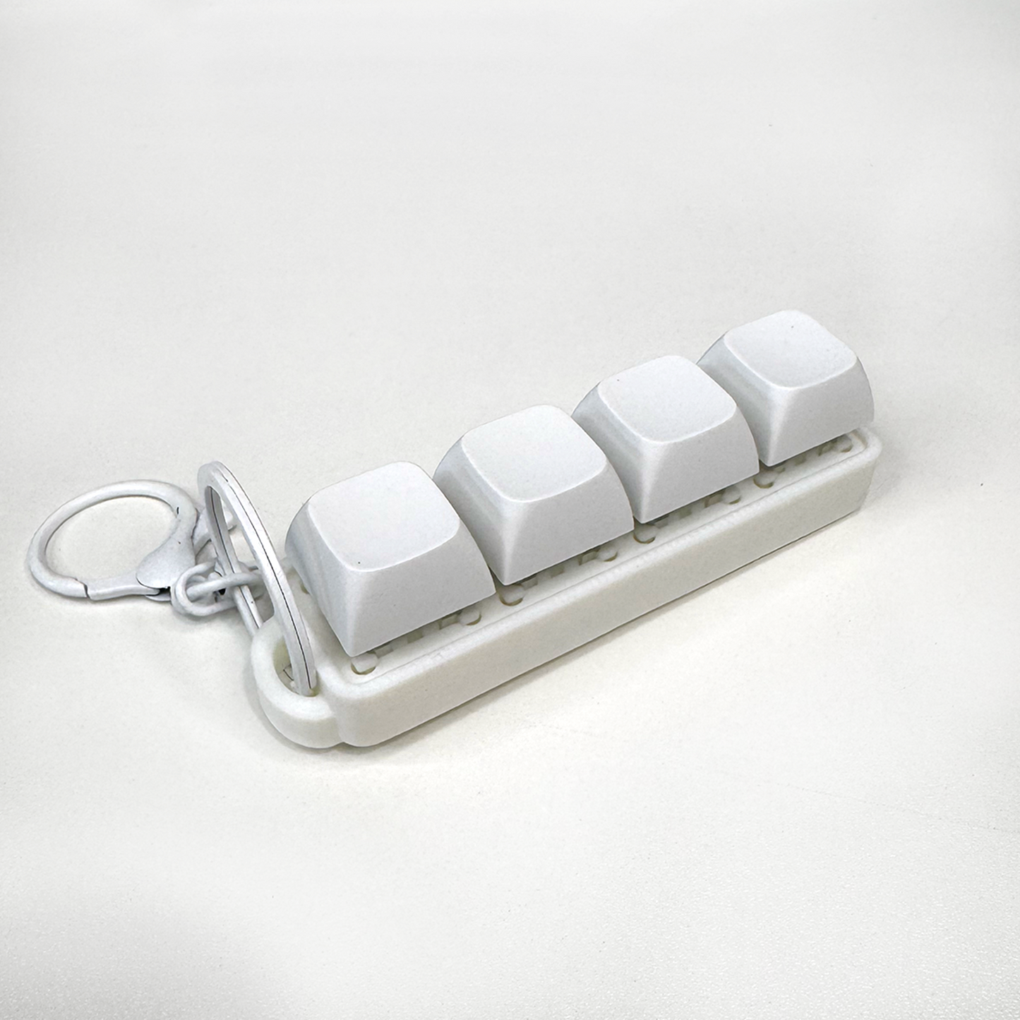 A white four-button clicker fidget keychain with a keychain ring, made with a biodegradable, plant-based plastic.